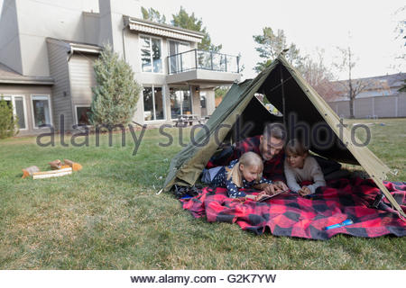 Père et filles using digital tablet in backyard tente