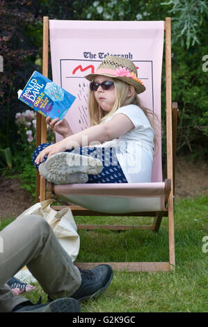 Jeune fille assise dans une chaise longue lecture du livre sur la pelouse à l'Hay Festival 2016 Banque D'Images