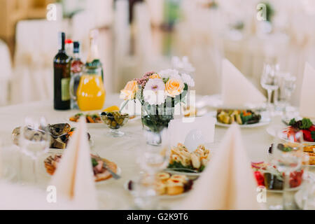 Restaurant banquet servi finement avec des collations, des couverts de table, vin, verres et une décoration florale. La nourriture européenne Banque D'Images