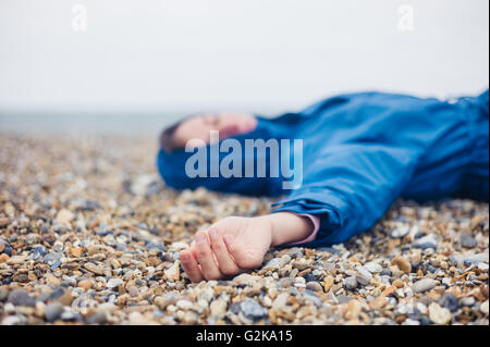 Une femme inconsciente est allongé sur une plage de galets Banque D'Images