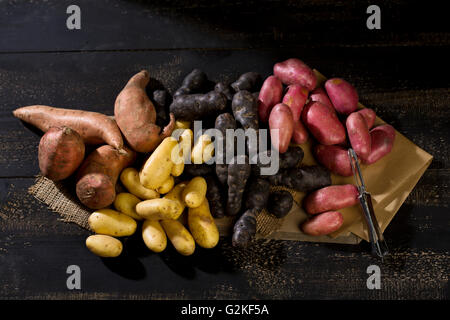 Différentes sortes de pommes de terre et peeler sur du papier brun, le jute et le bois foncé Banque D'Images