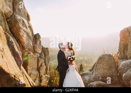 Portrait of romantic newlywed couple va baiser dans le coucher du soleil sur les feux de montagnes avec de gros rochers comme contexte Banque D'Images