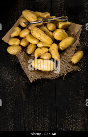 Matières Cherie pommes de terre et peeler sur du papier brun, le jute et le bois foncé Banque D'Images