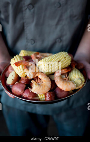 Chef Holding Assiette de Pays à faible ébullition avec les crevettes, le maïs, les pommes de terre et des saucisses Banque D'Images