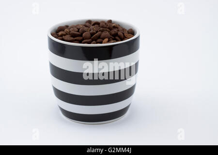 Mug blanc et noir plein de grains de café brun sur fond blanc Banque D'Images