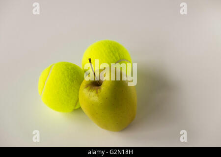 Jaune d'apple en face de deux balles de tennis sur fond blanc Banque D'Images