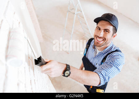 Close-up portrait of a handsome builder à l'aide de rouleau à peindre dans son travail à l'intérieur Banque D'Images