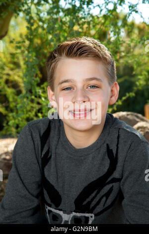 Portrait d'un garçon blond, le tween souriant à l'appareil photo à l'extérieur. Banque D'Images