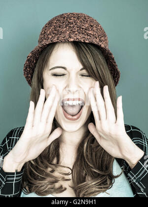 Tonique Portrait d'une jeune femme portant un bonnet de laine rouge crier ou hurler à l'appareil photo avec les yeux fermés Banque D'Images