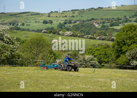 Le hersage garçon un champ avec son quad sur une journée ensoleillée. Arrière-plan de collines anglais. Banque D'Images