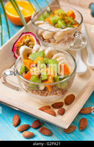 Petit-déjeuner diététique. Muesli, yaourt, fruits tropicaux : mangue, kiwi, ananas, fruits de la passion dans des gobelets et des amandes. Banque D'Images