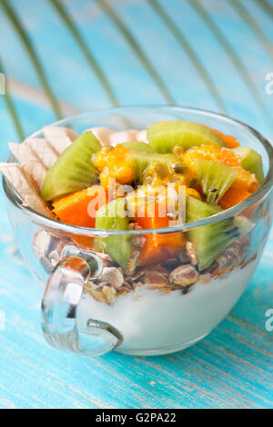 Petit-déjeuner diététique. Muesli, yaourt, fruits tropicaux : mangue, kiwi, ananas, fruits de la passion dans la tasse sur un fond bleu Banque D'Images