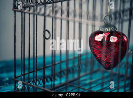 Coeur rouge coincé dans un vieux rusty cage à oiseaux Banque D'Images