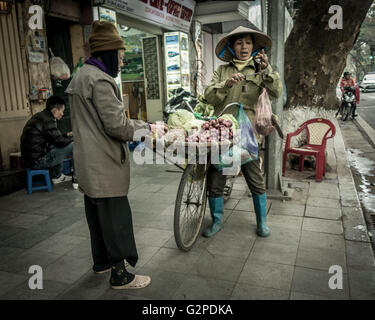 Femme sur un vélo la vente de légumes frais, à l'aide de balances traditionnelles portant des vêtements traditionnels de la culture locale, Hanoi, Vietnam Banque D'Images