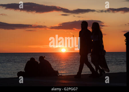 Pays de Galles, Aberystwyth Royaume-uni Bank Holiday Lundi, 01 juin 2016 UK Weather : Personnes en silhouette sur Aberystwyth promenade, derrière eux, les soleils définit de façon spectaculaire sur la baie de Cardigan au bord de la mer à Aberystwyth, sur la côte ouest du pays de Galles. Le temps a été beau et chaud sur la côte ouest, contrairement à la tempête de pluie et de l'expérience de Londres et de l'est Crédit photo : Keith Morris / Alamy Live News Banque D'Images