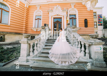 Belle robe de mariée dans de magnifiques avec longue queue qui monte l'escalier en pierre à l'édifice d'époque romantique Banque D'Images