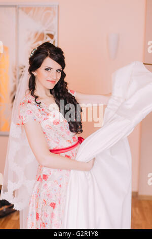 Pretty young girl holding wedding gown in dressing, préparation de l'habiller pour son mariage Banque D'Images