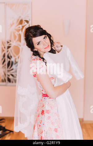 Pretty young girl holding silk wedding gown in dressing, préparation de l'habiller pour son mariage Banque D'Images