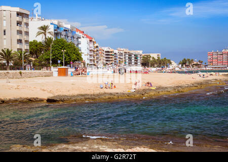 Plage méditerranéenne ensoleillée, les touristes vous détendre sur le sable chaud des chaises longues et des parasols. Les gens se baignent dans l'eau salée, Torrevieja Banque D'Images