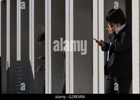 Des ouvriers de bureau ou des salarymen japonais fument à l'extérieur d'un bâtiment à Jimbocho, Tokyo, Japon. Banque D'Images