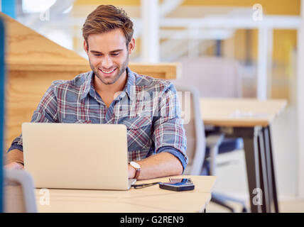 Hot man smiling alors qu'il travaille sur son ordinateur portable Banque D'Images