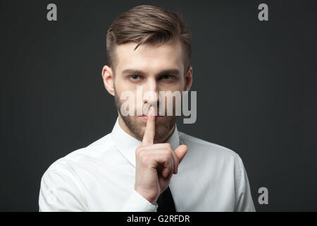 Gardez vos secrets ! Young handsome businessman gesturing 'shh' pour l'appareil photo. Banque D'Images