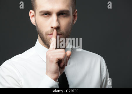 Gardez vos secrets ! Young handsome businessman gesturing 'shh' pour l'appareil photo. Banque D'Images