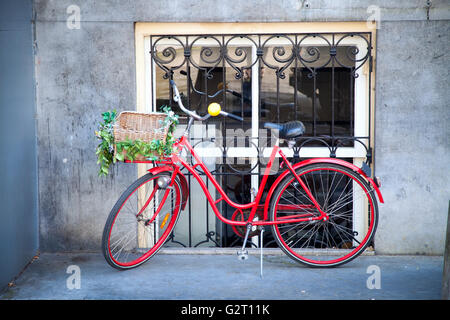 Vélo rouge avec des fleurs dans un panier placé sur la rue près de la maison Banque D'Images