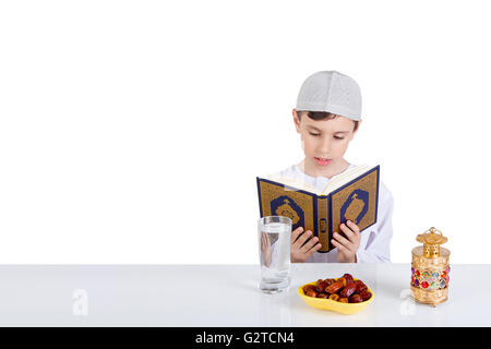 Jeune garçon musulman lecture Quraan en Ramadan - assis à une table avec de l'eau , dates , Coran, et Ramadan lantern Banque D'Images