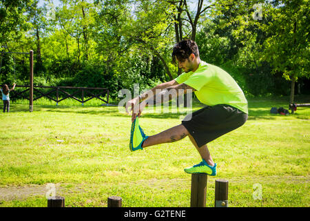 Vue latérale du dark-haired sportsman faisant pistol squats sur barre en bois dans la région de park Banque D'Images