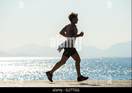 RIO DE JANEIRO - 3 avril, 2016 : un jeune carioca Brazilian jogger passe devant l'aube, la mer étincelante plage de Copacabana. Banque D'Images