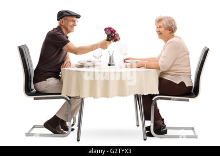 Homme mature donnant des fleurs à sa femme assis sur une date à une table isolé sur fond blanc Banque D'Images