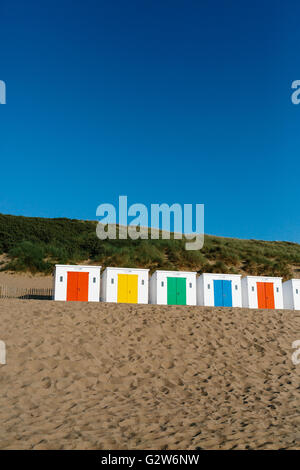 Une rangée de cabines de plage blanc avec portes colorées sur la plage de Woolacombe, Devon sur une journée ensoleillée Banque D'Images