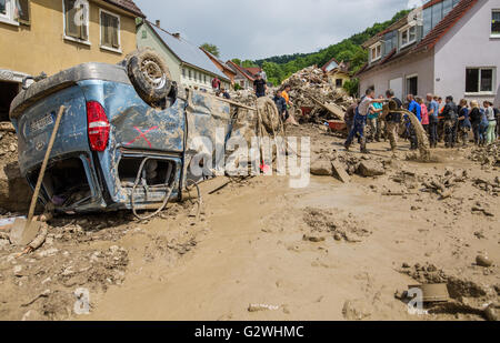 Braunsbach, Allemagne. 04 Juin, 2016. Helpers ont formé une chaîne pour enlever autant que possible la boue d'un bâtiment à l'aide de seaux locaux, avec une voiture accidentée située sur son toit, représenté à l'avant-plan, à Braunsbach, Allemagne, 04 juin 2016. Près d'une semaine après un gros orage, les opérations d'assainissement à Braunsbach fonctionnent à pleine vitesse. Photo : CHRISTOPH SCHMIDT/dpa/Alamy Live News Banque D'Images