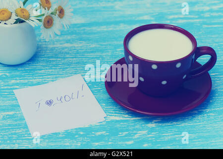 Fleurs Daisy et tasse de lait avec un bon matin note sur fond de bois bleu rustique Banque D'Images