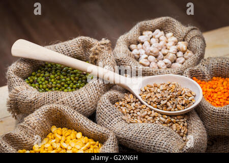 Sacs de jute avec des pois secs, pois chiches, lentilles, blé rouge et vert mung sur table de cuisine Banque D'Images