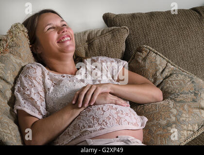 Smiling pregnant woman sitting on a sofa et caressant son ventre Banque D'Images