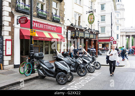 Une jeune femme, avec un téléphone mobile à la main, passe devant des Spaghetti House sur St Martins Lane, London, WC2H, UK Banque D'Images