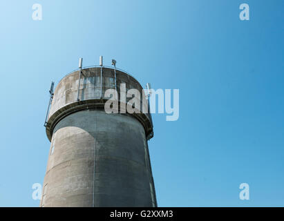 Tour d'eau en béton coulé très abîmé, vu contre un ciel bleu clair. Les mâts de télécommunication 5G récemment installés sont visibles au sommet de la tour. Banque D'Images