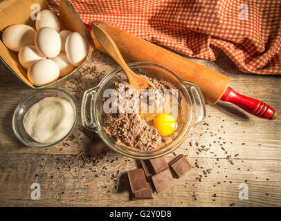 La confection d'un gâteau au chocolat. Préparer la pâte à gâteau au chocolat entouré par des ingrédients frais, une cuillère de bois et de chocolat. Banque D'Images