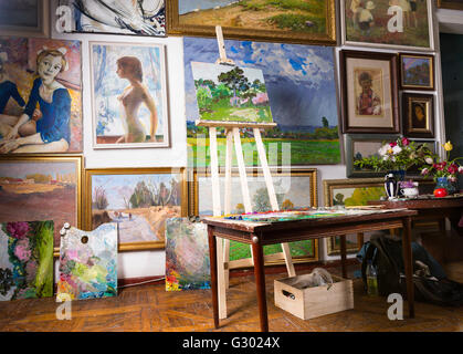 Intérieur d'un studio ou une galerie de peintres avec des toiles couvrant une variété de sujets accroché au mur et un tableau sur un chevalet en bois. Banque D'Images