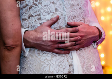 Un groom's les mains et les bras autour de la taille de son épouse au cours de la soirée de danse à un mariage. Banque D'Images