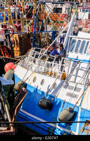 Deux membres d'équipage philippins sur le côté d'un chalutier dans un port très fréquenté. Banque D'Images