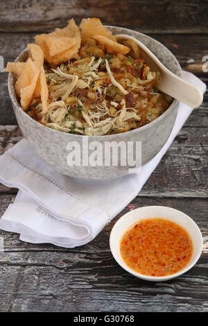 Bubur Ayam. Poulet porridge fancily Peranakan Bol en céramique contemporaine plaqué ; puis bordée de serviette en lin blanc. Organisé sur table rustique. Banque D'Images