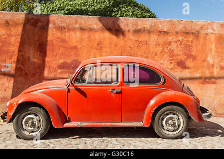 Une vieille Volkswagen Coccinelle rouge voiture garée contre un mur rouge dans le centre historique de San Miguel de Allende, Mexique. Banque D'Images