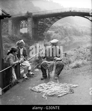 Le coracle et braconnier Harry Rogers réparant ses filets de pêche surveillés par deux jeunes filles à Ironbridge, Shropshire 1960 Grande-Bretagne Banque D'Images