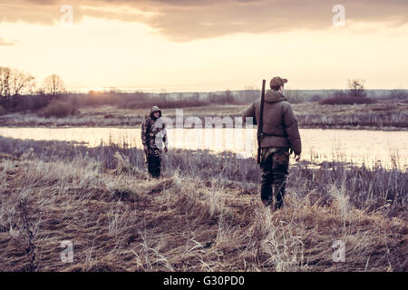 Les chasseurs le choix d'un bon poste pour la chasse aux canards dans le champ à proximité de la rivière au lever du soleil Banque D'Images