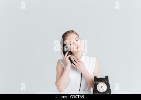 Relaxed woman with closed eyes parlant au retro phone isolé sur fond blanc Banque D'Images