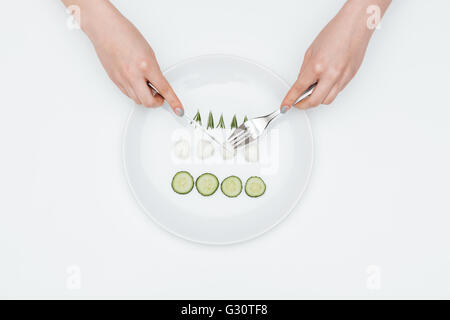 Vue de dessus de jeune femme coupe les mains et manger le concombre, mozzarella et les herbes sur la plaque sur fond blanc Banque D'Images