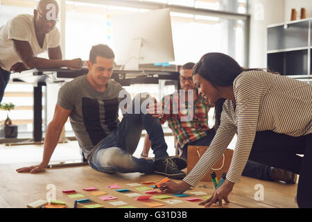 Groupe de quatre employés séance autour de diverses notes adhésives de couleur sur plancher de petit bureau Banque D'Images